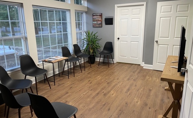 Interior reception area with black chairs, wooden flooring, large windows with blinds, and white doors
