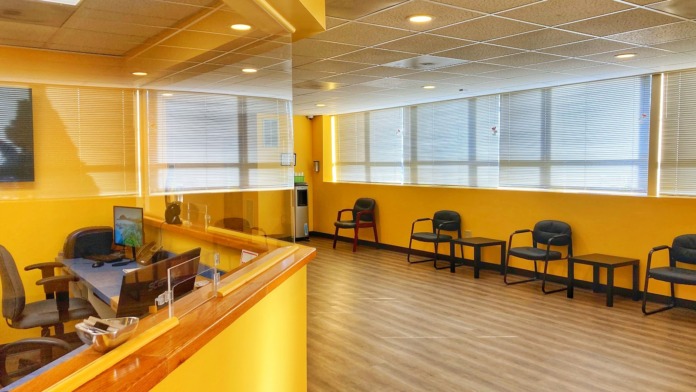 Interior reception area with yellow walls, desk, waiting chairs, windows, and modern lighting fixtures