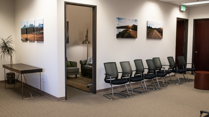 Interior reception area with rows of gray mesh office chairs, landscape wall art, glass-walled office, and minimalist furnishings
