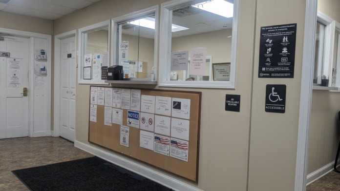 Interior reception area with cream walls, window counter with bulletin board, black entry mat, and adjacent office doors