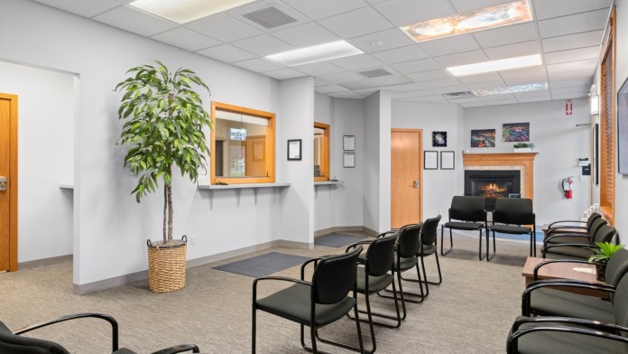 Interior common space with rows of black chairs, fireplace, potted plant, window with blinds, and framed artwork