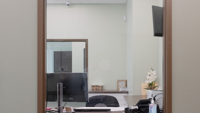 Interior reception window with wooden frame and office workspace visible through glass partition