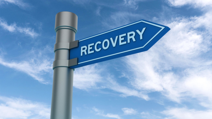 Outdoor directional signpost with blue recovery arrow sign against sky with clouds