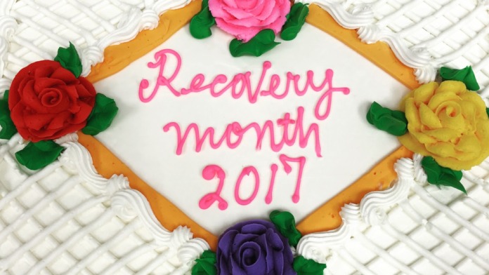 Decorated celebration cake with frosting, sugar flowers, and Recovery Month 2017 text in pink.