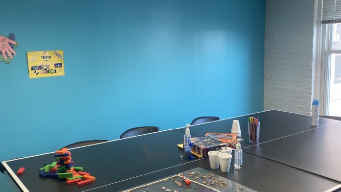 Interior activity space featuring blue accent walls, tables with puzzles and games, and natural window lighting