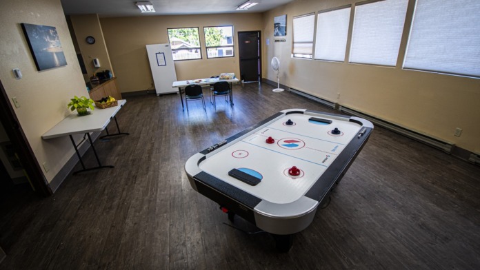 Interior recreation room featuring air hockey table, whiteboard, tables, chairs, and large windows with natural light