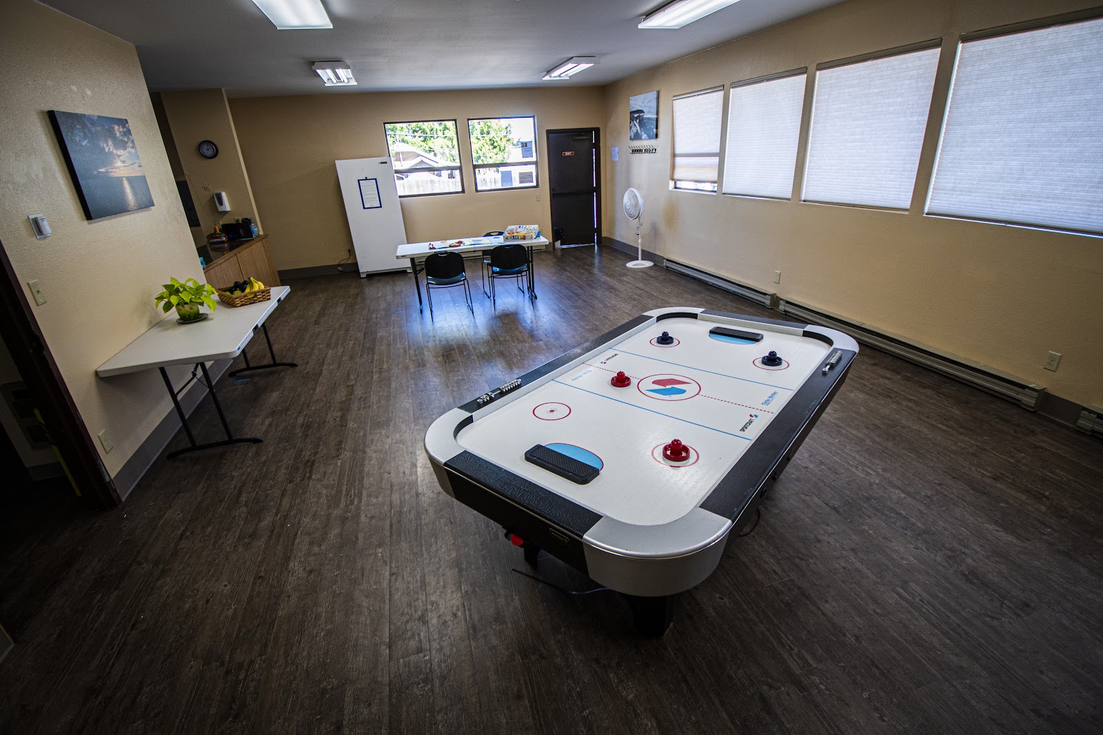 Interior recreation room featuring air hockey table, whiteboard, tables, chairs, and large windows with natural light