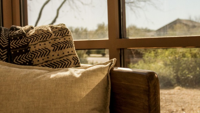 Interior seating nook with upholstered sofa, patterned pillows, and large windows viewing landscaped grounds.