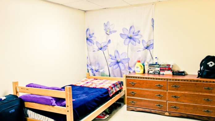 Interior bedroom with wooden bed frame, purple bedding, wooden dresser, wall tapestry, and personal items