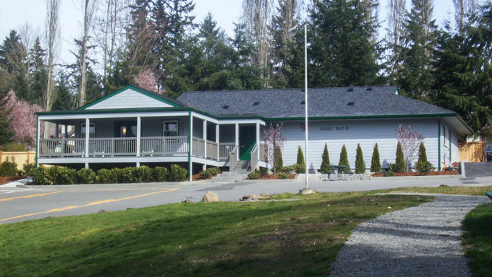 Exterior of residential-style treatment building with covered porch, white railings, landscaping, and connected structures