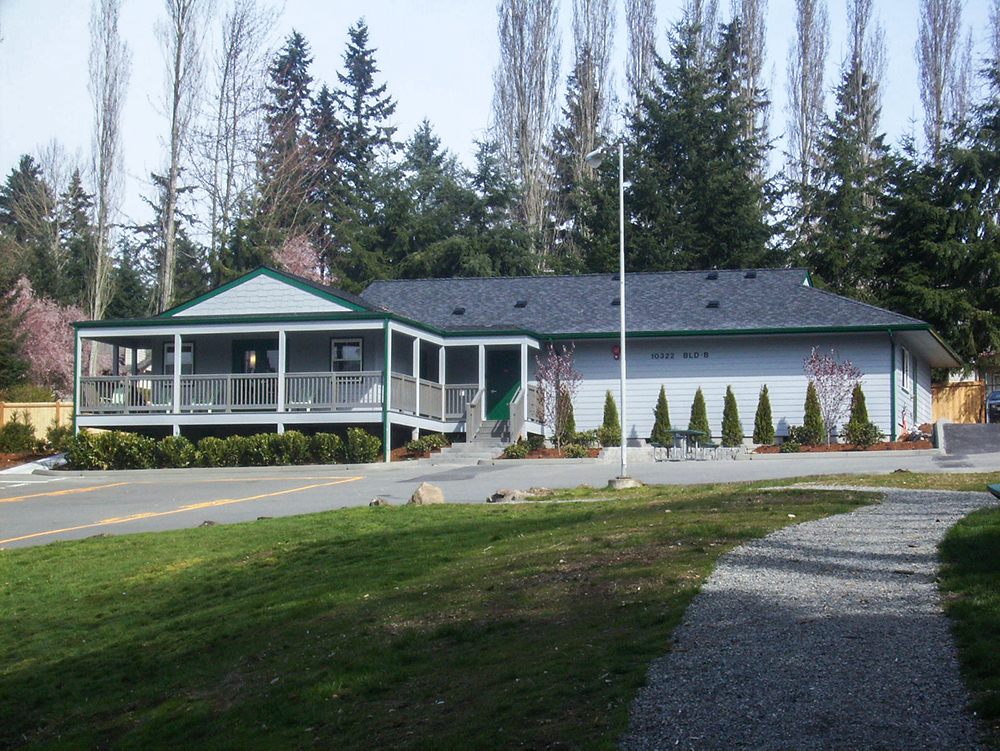 Exterior of residential-style treatment building with covered porch, white railings, landscaping, and connected structures
