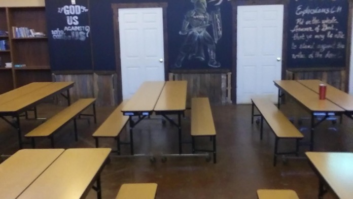 Interior dining space with picnic-style seating, tables with benches, and religious wall signage