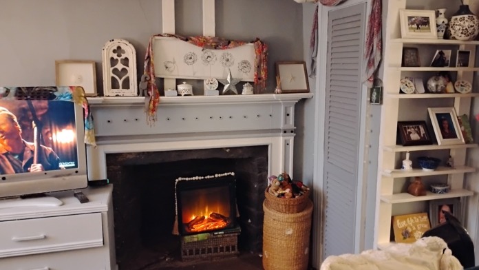 Interior room with electric fireplace, white shelving unit, framed artwork, decorative elements, and comfortable seating area