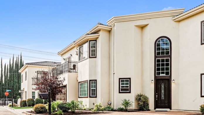 Exterior view of multi-story residential complex with pool, manicured lawn, and surrounding gardens