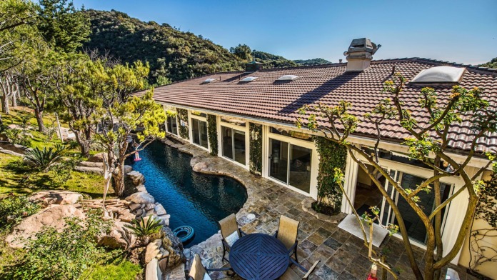 Exterior showing resort pool with lounge seating, stone patio, modern building facade, and hillside backdrop with mature landscaping