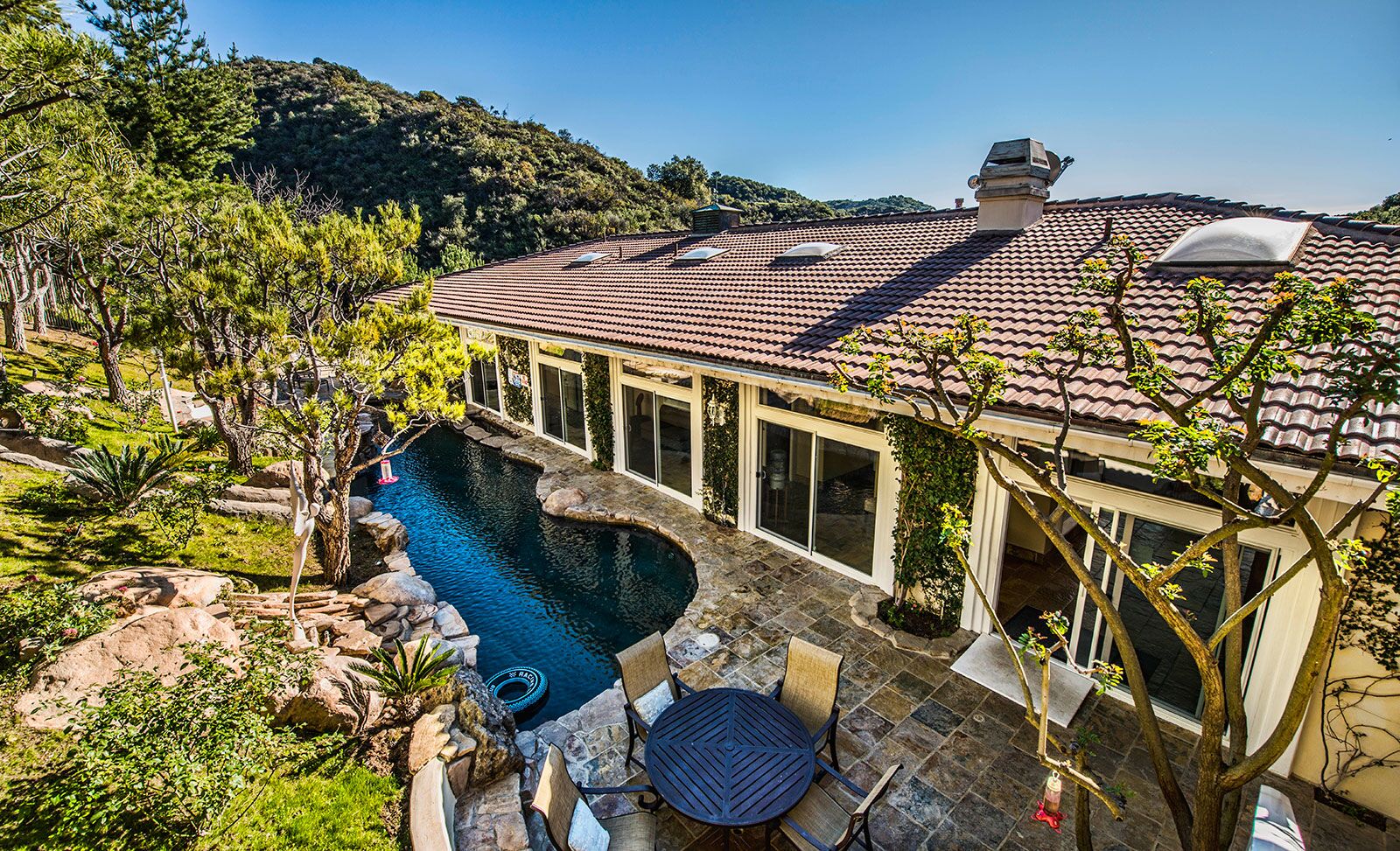 Exterior showing resort pool with lounge seating, stone patio, modern building facade, and hillside backdrop with mature landscaping