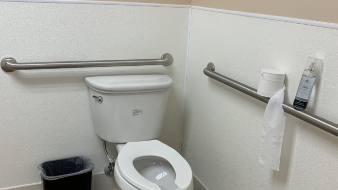 Interior restroom with toilet, grab bars for accessibility, paper towel dispenser, and spray bottle on sink area