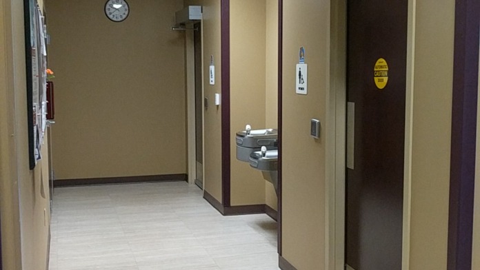 Interior restroom corridor with multiple stall doors, wall clock, and accessible fixtures