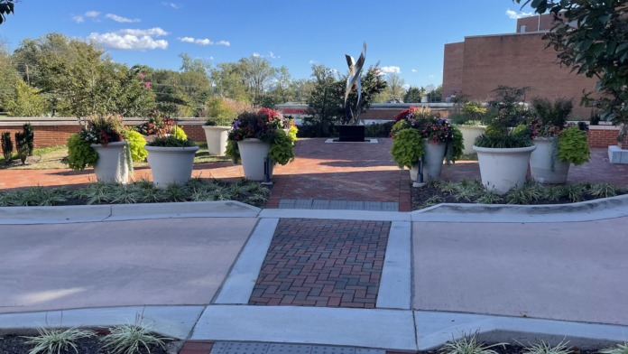 Exterior courtyard space with decorative planters, seasonal flowers, central sculpture art installation, and brick patio