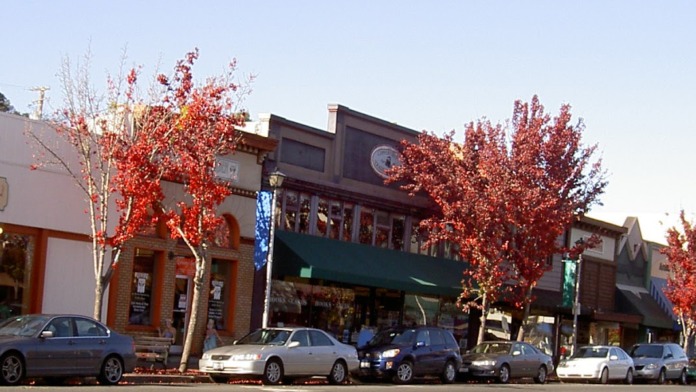 Exterior street view of downtown area with storefronts, parked cars, and red fall foliage trees