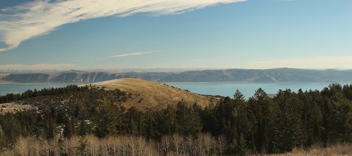 Exterior landscape view showing forested mountains, lake, and distant valleys under clear sky
