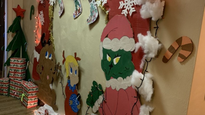 Interior entryway with illuminated holiday decorations, wrapped gift boxes, and festive wall art