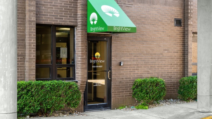 Exterior brick facade showing BrightView entrance with green awning, landscaping, and facility address number