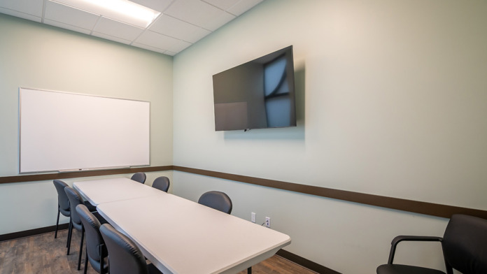 Interior training room with rectangular conference table, whiteboard, flat-screen monitor, and multiple participant seating