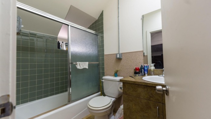 Interior bathroom with green tile shower enclosure, toilet, vanity, mirror, window, and storage items