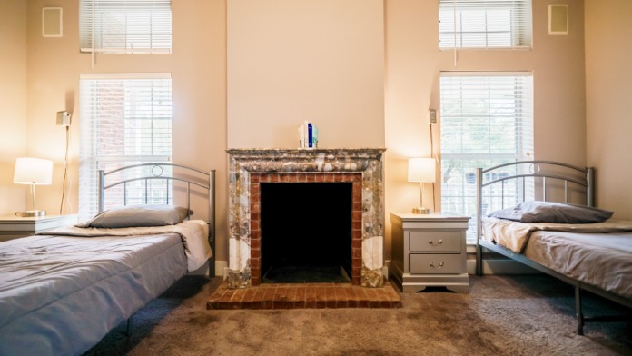 Interior bedroom with twin beds, fireplace, windows with blinds, lamps and warm neutral décor