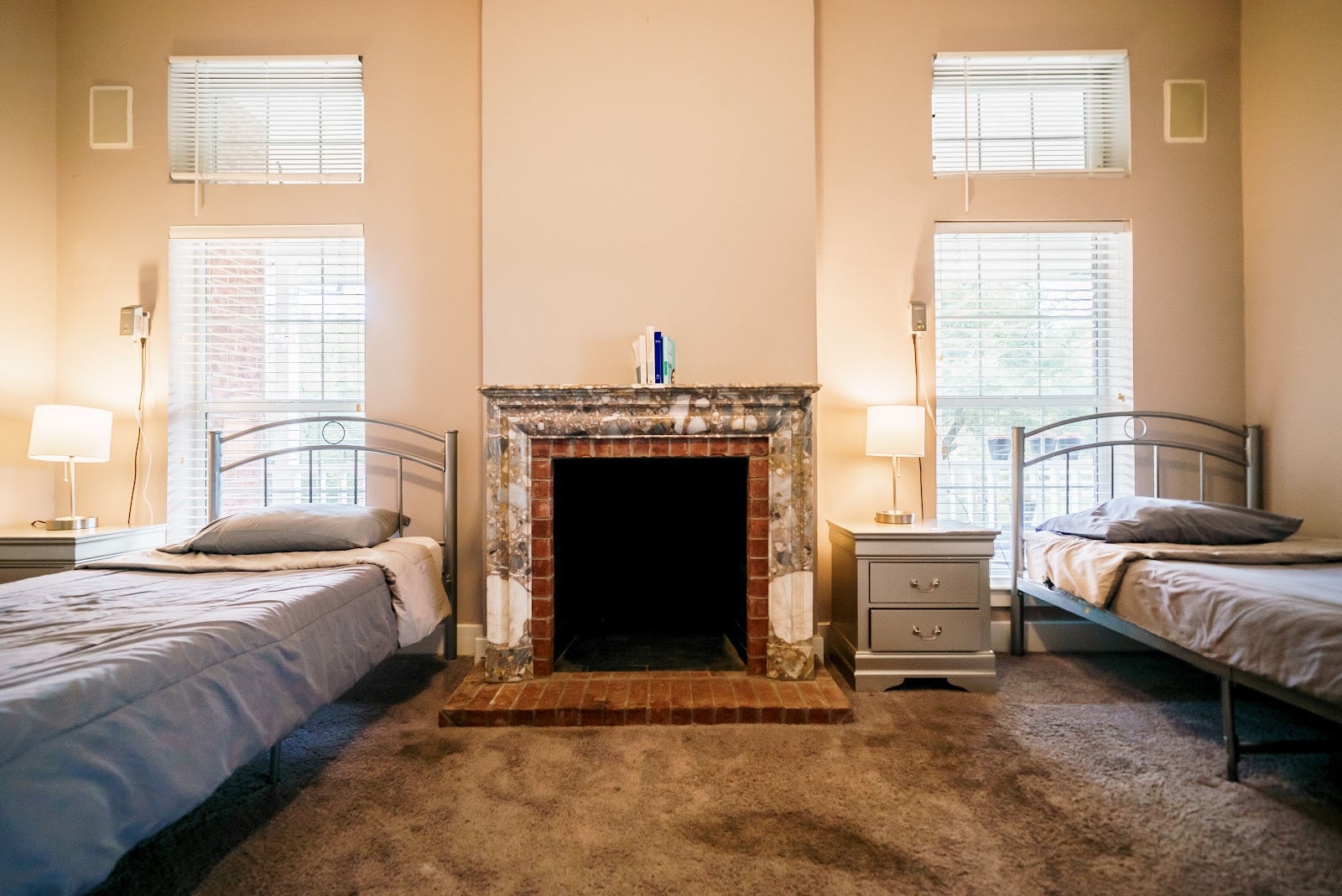 Interior bedroom with twin beds, fireplace, windows with blinds, lamps and warm neutral décor