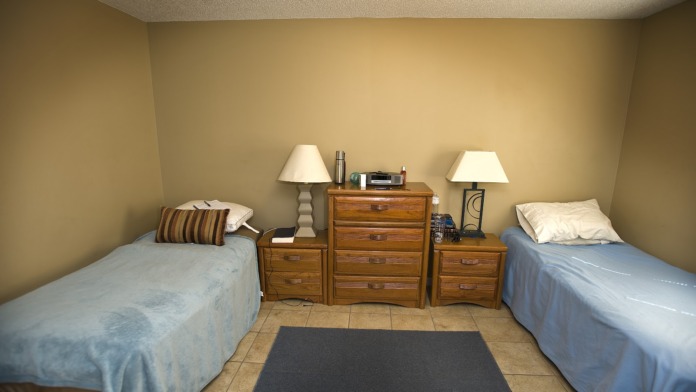 Interior bedroom with two twin beds, wooden nightstands, table lamps, and tile flooring