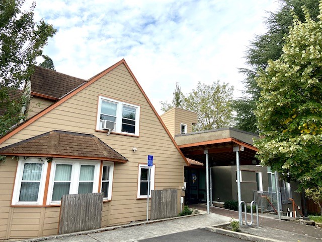 Exterior view of facility building with tan and brown siding, entrance door, windows, and surrounding landscaping