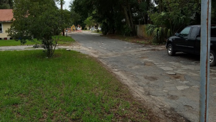 Exterior side view showing driveway approach, mature trees, landscaping, and parked vehicle near facility