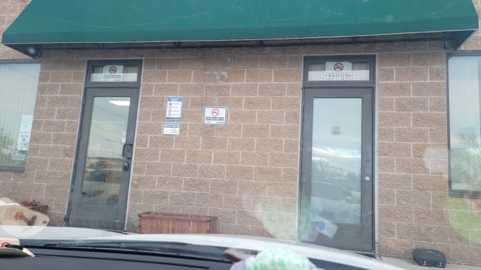 Exterior side entrance showing green awning, dark glass doors, no-smoking signage, and brick wall