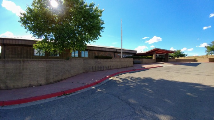 Exterior view of facility side entrance with brick walls, landscaping, flagpole, and parking area approach