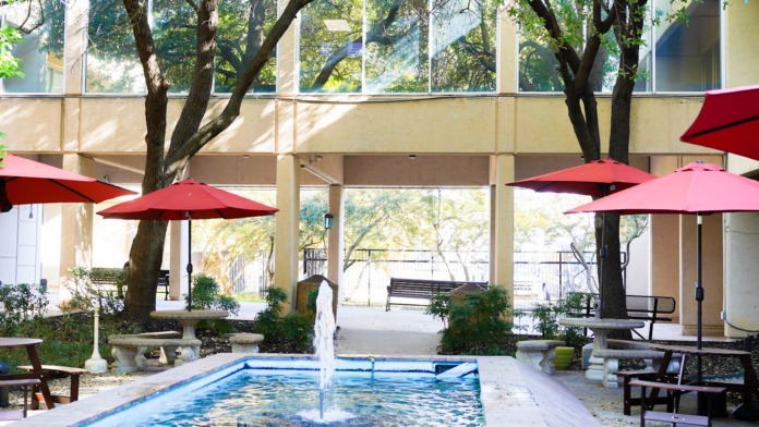 Exterior courtyard with hot tub, red umbrellas, shade trees, lounge furniture and facility building in background