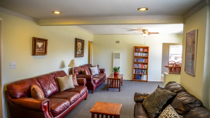 Interior common room featuring burgundy leather sofa, multiple comfortable seating areas, bookshelf, wall decorations, and natural window lighting
