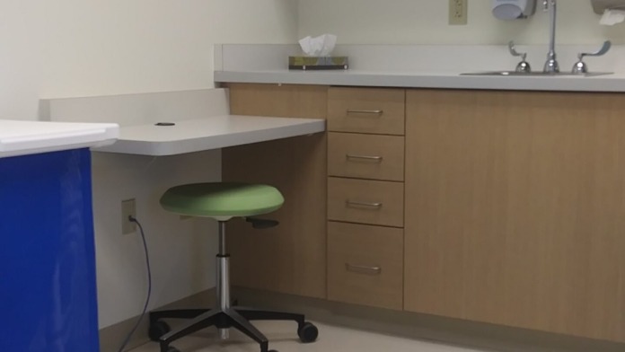 Interior clinical specimen collection area with examination chair, sink, cabinetry, and equipment for patient care procedures
