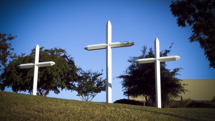 Outdoor grounds with three large white memorial crosses on grassy area with landscaping and facility building