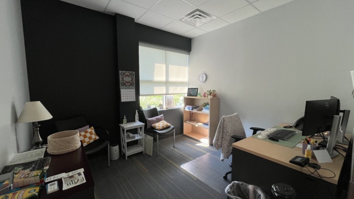 Interior office area with desk, computer monitor, black accent wall, natural window view, and seating area