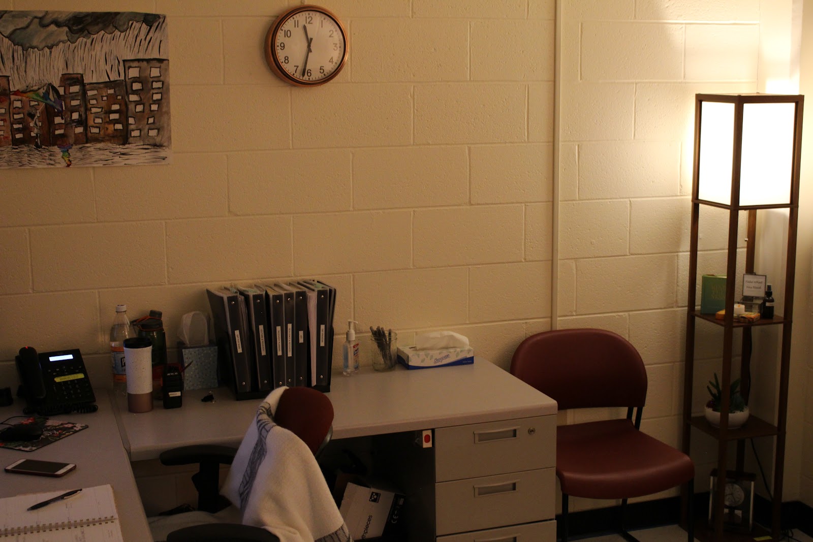 Interior office space with desks, computer equipment, file cabinets, wall clock, and framed artwork on cream-colored walls