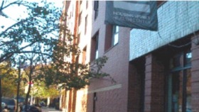 Exterior view of brick building facade with street-level windows and storefront entry on East 9th Street