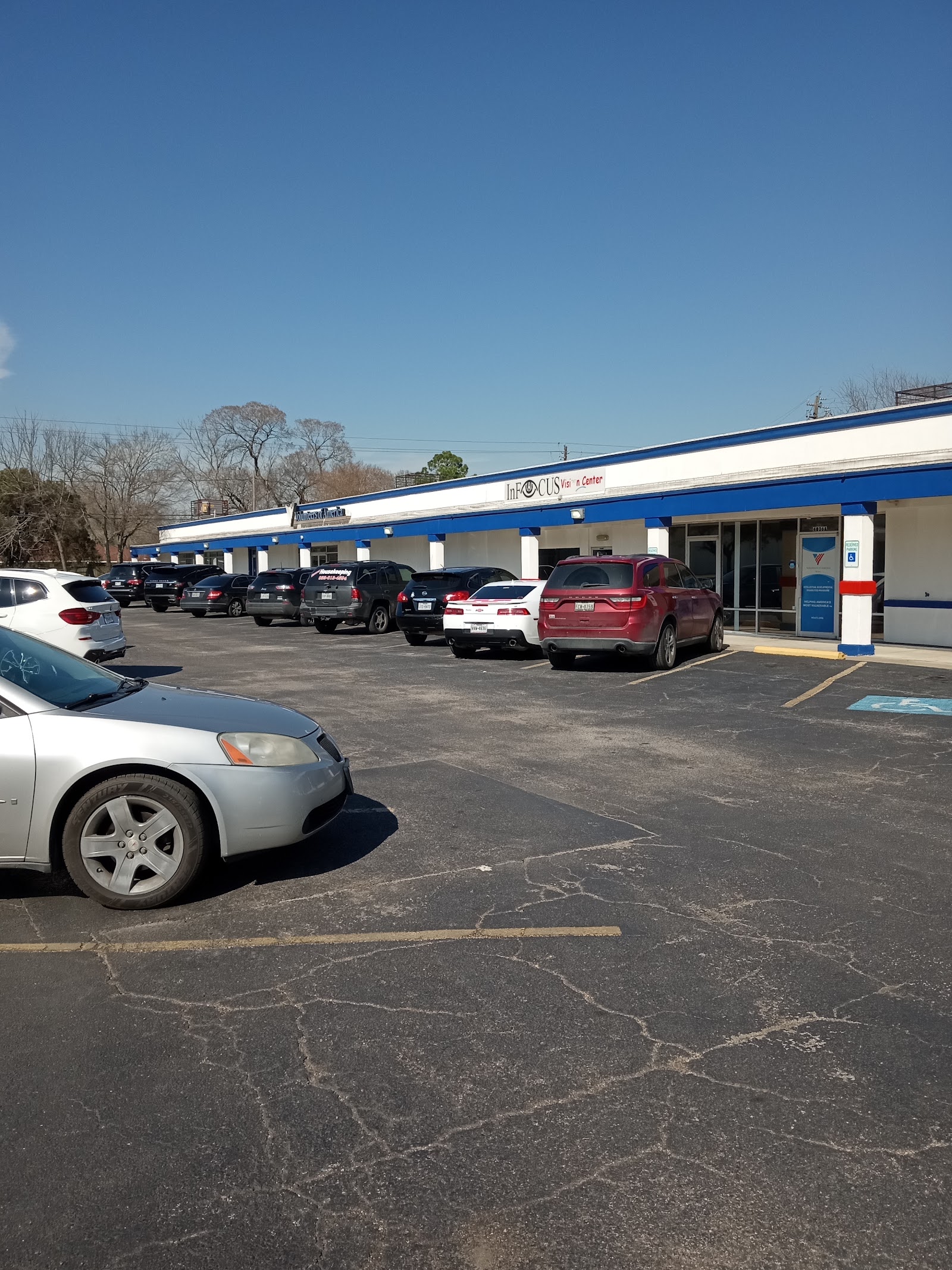 Exterior storefront with blue and white striped awning, parking lot with multiple vehicles