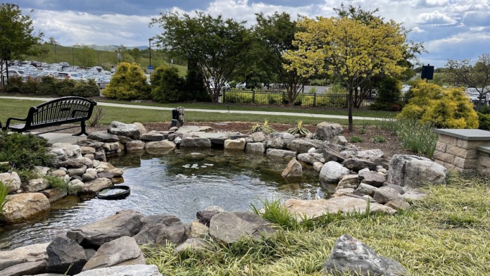 Outdoor garden space with rock-lined pond, benches, walking paths, landscaping, and mountain views in background