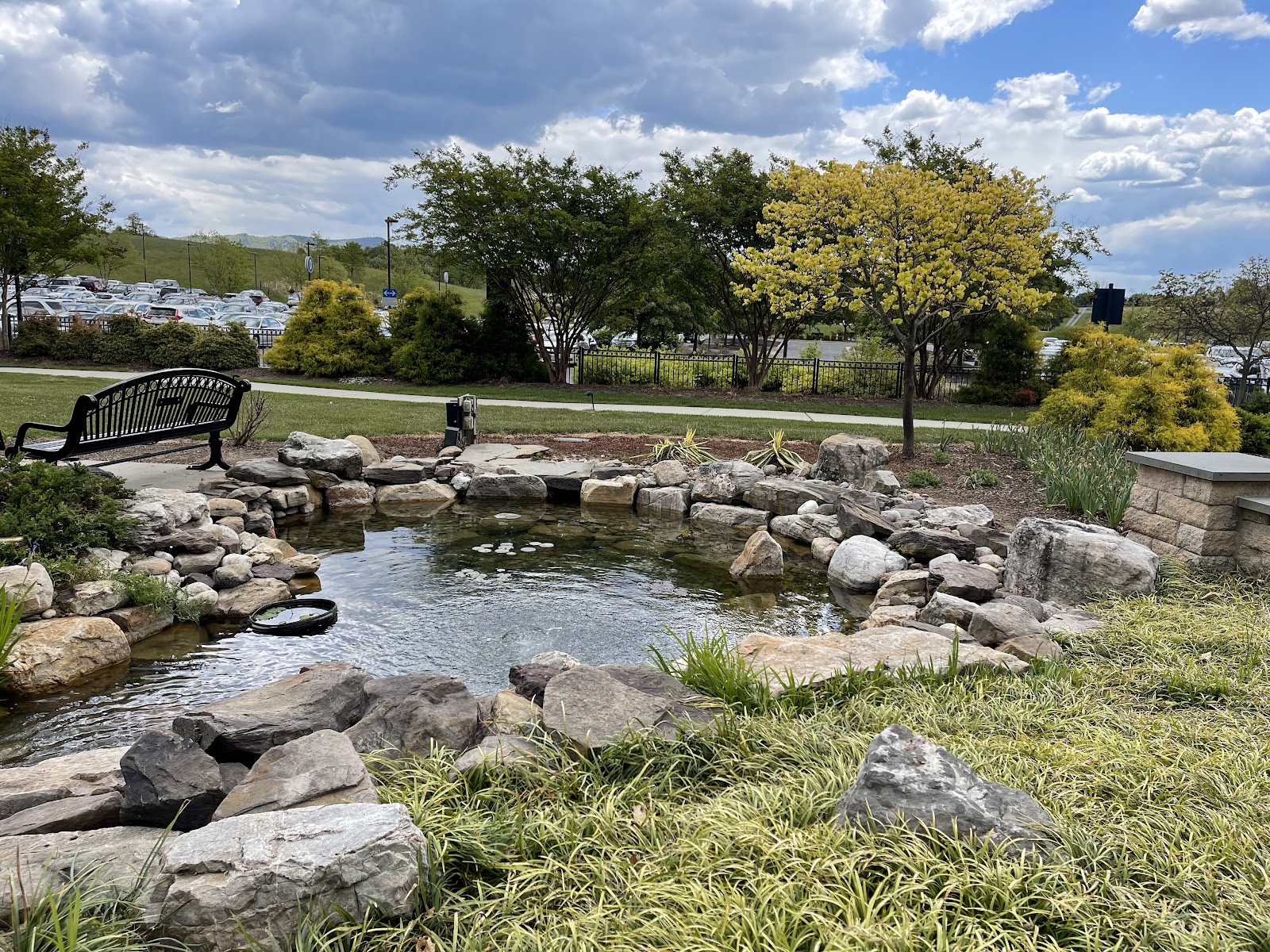 Outdoor garden space with rock-lined pond, benches, walking paths, landscaping, and mountain views in background