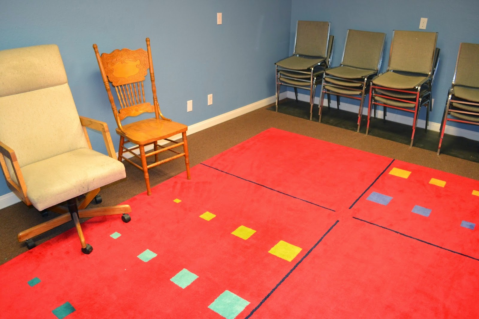 Interior activity space with red mat flooring, colored squares, wooden chairs, and motivational wall displays