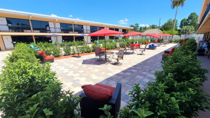 Exterior patio area with red umbrellas, comfortable seating, lush green plants, and facility building with windows