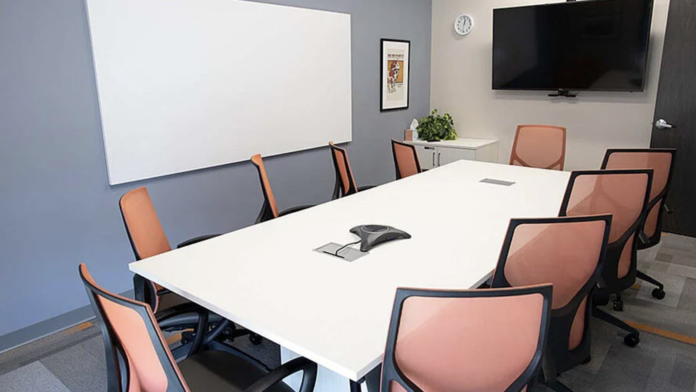 Interior therapy room with large conference table, orange office chairs, whiteboard, television, and clock on wall