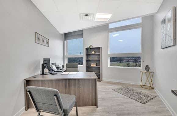 Interior therapy room with desk, office chair, bookshelves, whiteboard, and calming wall decor